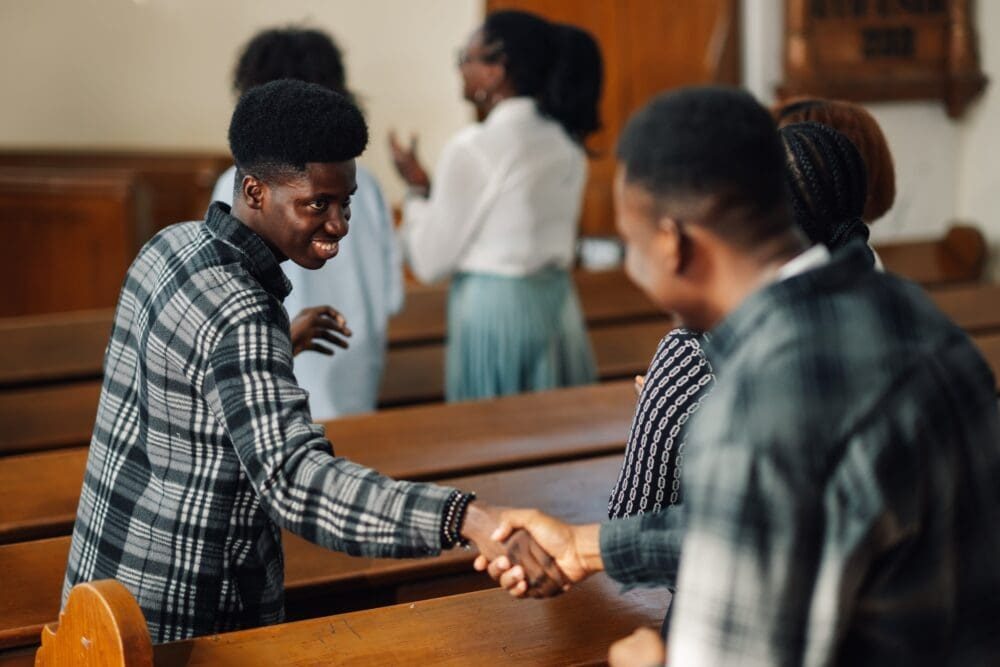 Two men shaking hands during church service with congregation in background